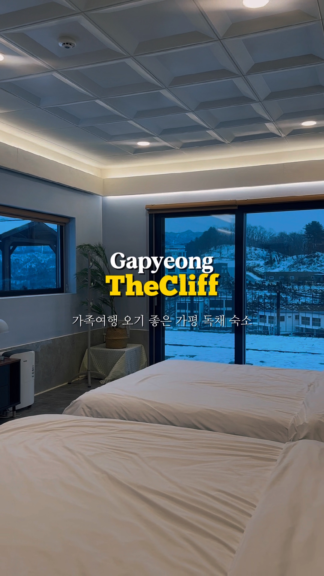 흰 침구가 덮인 침대와 창밖의 눈 덮인 풍경이 보인다