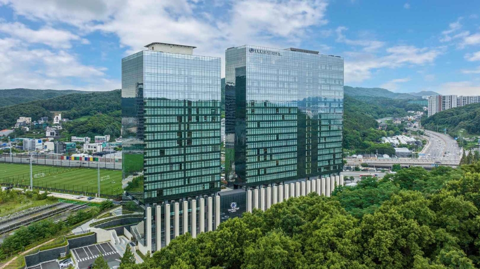 푸른 숲과 도로 옆에 자리한 유리 마감의 대형 호텔 건물 외관