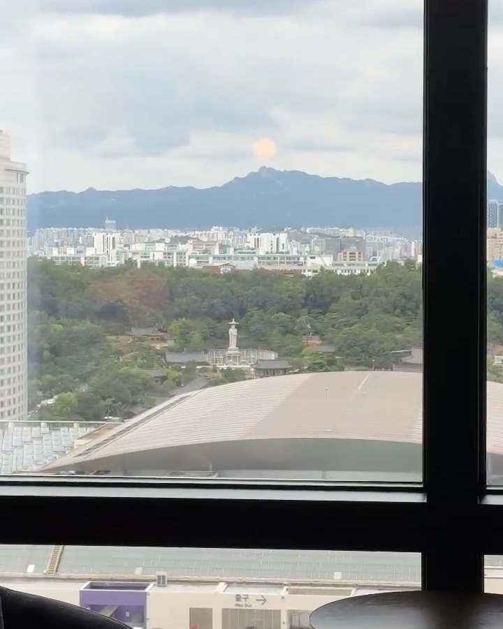 창밖으로 불상과 사찰, 도심 건물들과 산 능선이 내려다보이는 창가 전망입니다.