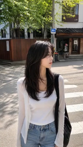 긴 검은 머리의 여성이 거리에서 옆을 바라보는 모습